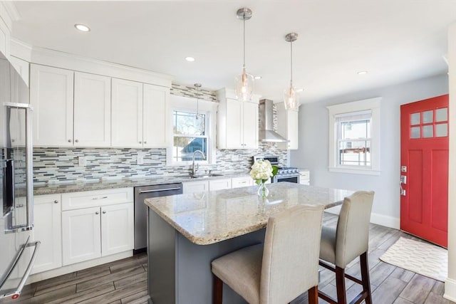 kitchen featuring stainless steel appliances, sink, wall chimney range hood, white cabinetry, and a kitchen island