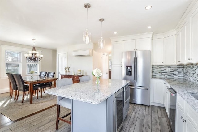 kitchen featuring stainless steel appliances, decorative light fixtures, white cabinetry, an AC wall unit, and a kitchen island