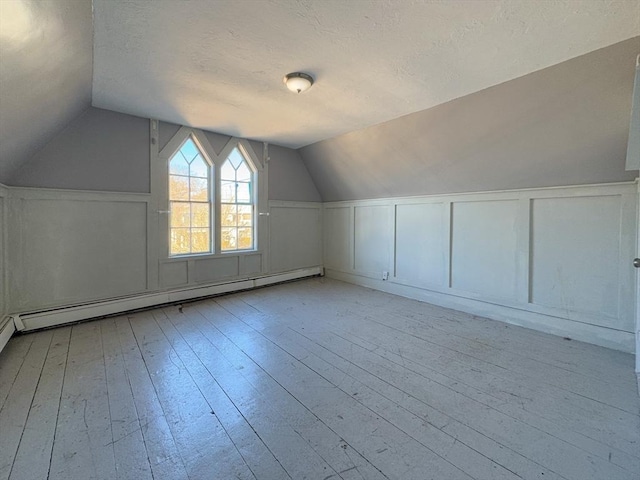 additional living space featuring vaulted ceiling, a textured ceiling, a baseboard radiator, and light hardwood / wood-style flooring