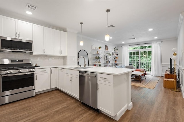 kitchen featuring visible vents, appliances with stainless steel finishes, a peninsula, crown molding, and a sink