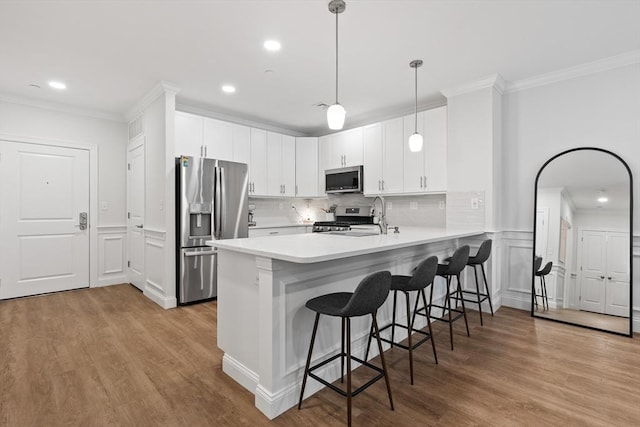 kitchen with appliances with stainless steel finishes, a breakfast bar, a peninsula, light countertops, and crown molding