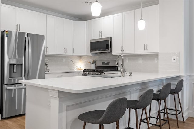 kitchen featuring stainless steel appliances, a peninsula, light wood-style flooring, and white cabinets