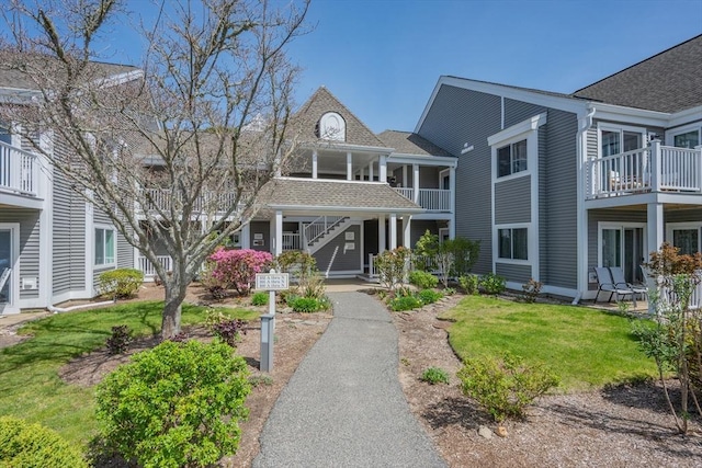 view of front of home with stairway, a shingled roof, a balcony, and a front yard
