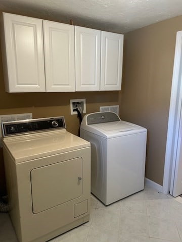 washroom with washer and dryer, light tile patterned floors, a textured ceiling, and cabinets