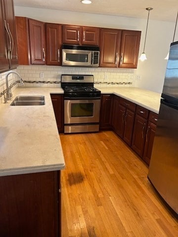 kitchen with decorative backsplash, light wood-type flooring, stainless steel appliances, sink, and pendant lighting