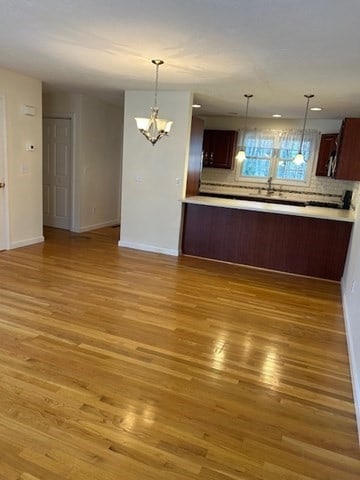 kitchen featuring tasteful backsplash, kitchen peninsula, light hardwood / wood-style floors, and an inviting chandelier