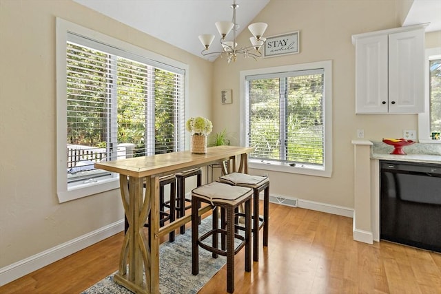 dining room with light wood-type flooring, lofted ceiling, a wealth of natural light, and a chandelier