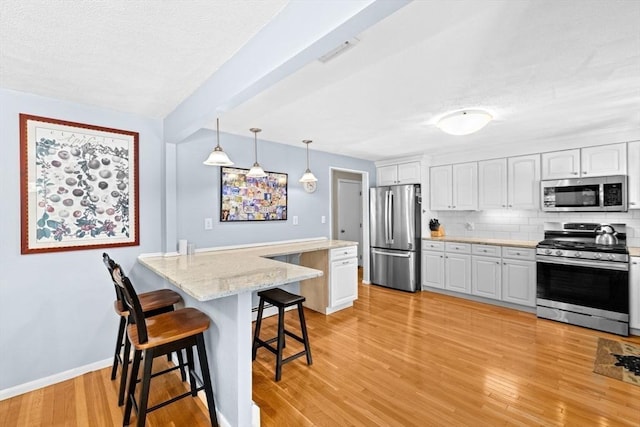 382 Tilden Rd, Scituate, MA 02066 - kitchen with stainless steel appliances, a breakfast bar area, a peninsula, decorative backsplash, and white cabinets