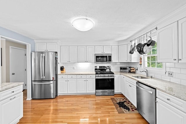 382 Tilden Rd, Scituate, MA 02066 - kitchen with stainless steel appliances, light wood finished floors, decorative backsplash, white cabinetry, and light stone counters