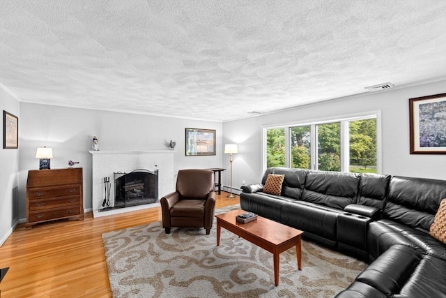 382 Tilden Rd, Scituate, MA 02066 - living room featuring a textured ceiling, light wood-style flooring, a brick fireplace, baseboard heating, and crown molding