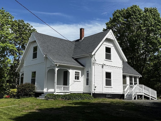 back of property with covered porch, roof with shingles, a chimney, and a yard