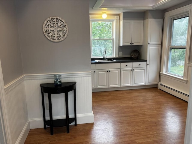 kitchen with a sink, baseboard heating, dark countertops, white cabinetry, and a wainscoted wall