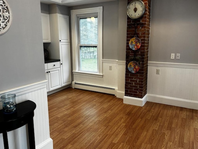 unfurnished dining area featuring baseboard heating, a wainscoted wall, and dark wood-style floors