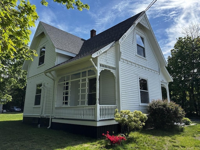 view of property exterior with covered porch, a chimney, a shingled roof, and a yard