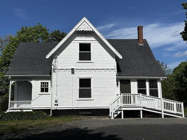 back of property featuring a porch, a shingled roof, and a chimney