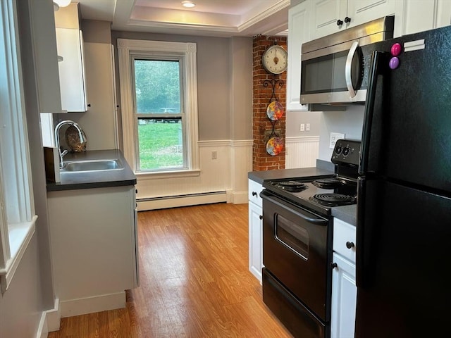 kitchen with black appliances, baseboard heating, a sink, dark countertops, and light wood-style floors