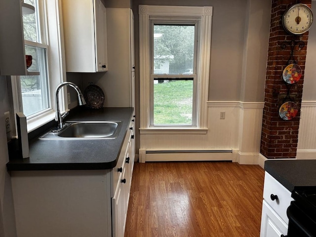 kitchen with a baseboard heating unit, dark countertops, a sink, white cabinets, and healthy amount of natural light