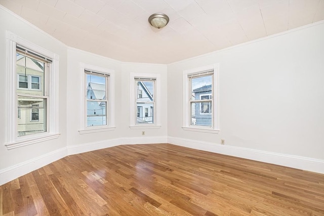 spare room featuring baseboards, a healthy amount of sunlight, light wood-style floors, and ornamental molding