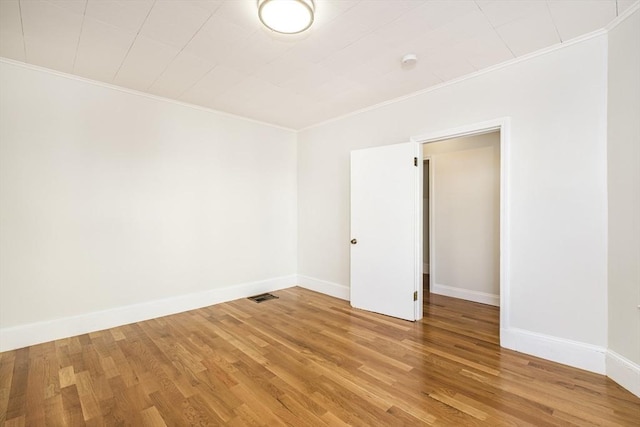 empty room featuring visible vents, baseboards, light wood-style flooring, and ornamental molding