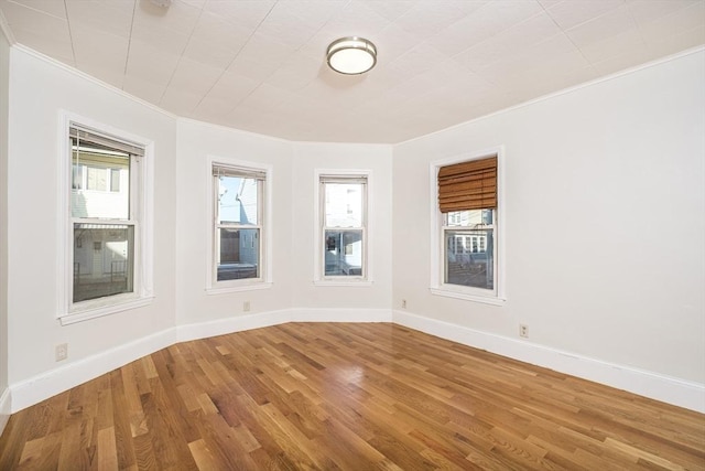 empty room with crown molding, wood finished floors, and baseboards