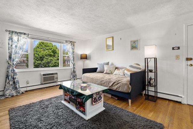 51 Warren St Unit 2-2, Waltham, MA 02453 - bedroom featuring an AC wall unit, baseboard heating, a textured ceiling, and wood finished floors