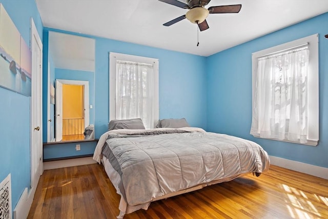 bedroom with baseboards, a ceiling fan, wood finished floors, and multiple windows