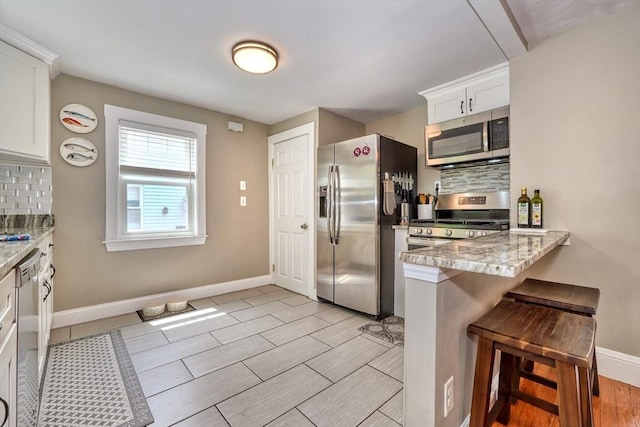 215 Curve, Dedham, MA 02026 - kitchen featuring stainless steel appliances, backsplash, a kitchen breakfast bar, white cabinetry, and baseboards
