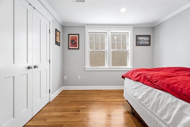 bedroom featuring visible vents, baseboards, light wood-style floors, and ornamental molding