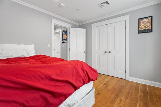 bedroom with visible vents, wood finished floors, a closet, crown molding, and baseboards