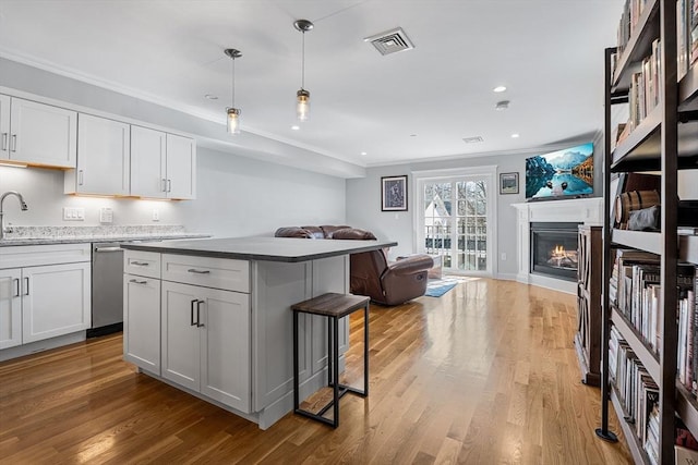 kitchen with visible vents, light wood-style floors, a glass covered fireplace, crown molding, and open floor plan