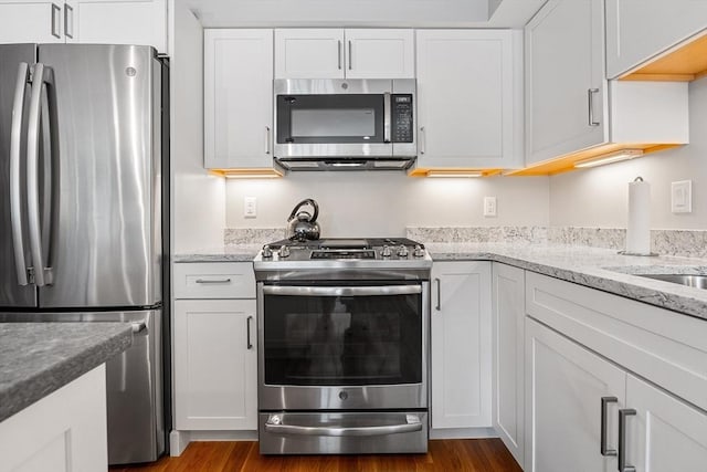 kitchen featuring dark wood-style flooring, appliances with stainless steel finishes, white cabinetry, and light stone countertops