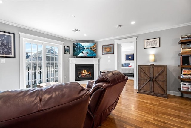 living area with visible vents, wood finished floors, a glass covered fireplace, crown molding, and baseboards