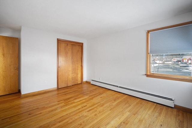 unfurnished bedroom featuring a baseboard heating unit, light wood-type flooring, and a closet