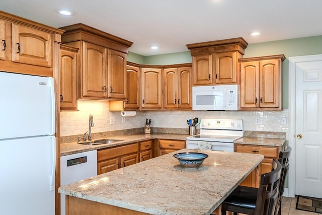 kitchen with a center island, white appliances, a kitchen breakfast bar, sink, and light stone countertops