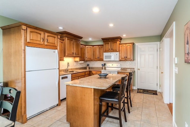 kitchen featuring a kitchen breakfast bar, white appliances, sink, light tile patterned floors, and a center island