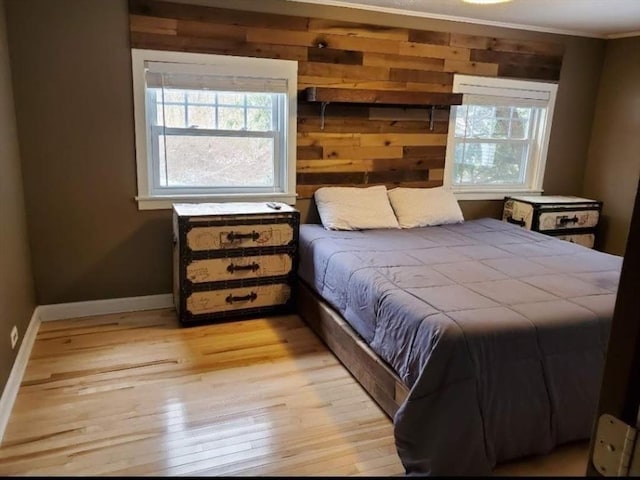 bedroom with multiple windows, light hardwood / wood-style flooring, ornamental molding, and wooden walls