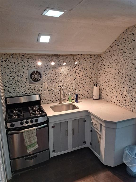 kitchen with sink, vaulted ceiling, gray cabinetry, a textured ceiling, and range with gas cooktop