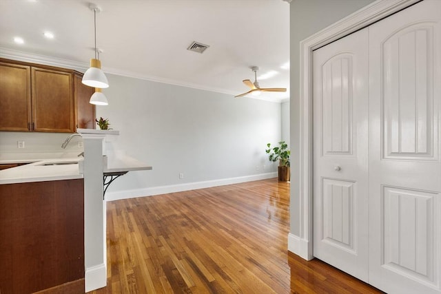 interior space featuring crown molding, a sink, light countertops, a ceiling fan, and wood finished floors