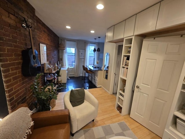 living area featuring light wood-style flooring, recessed lighting, brick wall, and baseboards