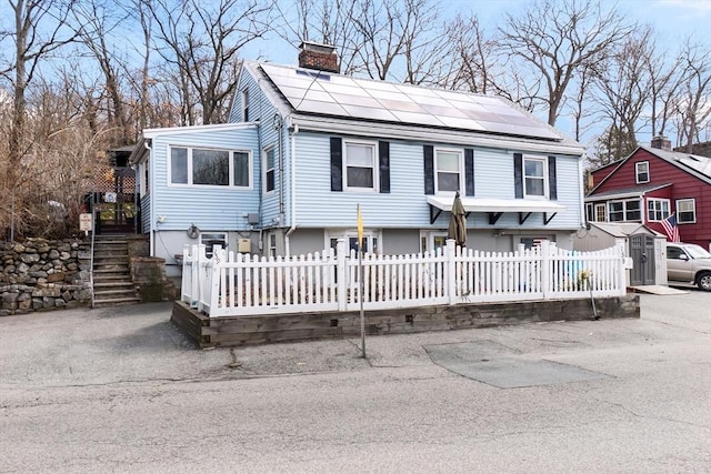 view of front of house with roof mounted solar panels, a chimney, and a fenced front yard