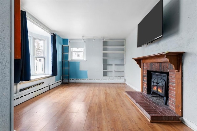 unfurnished living room with wood-type flooring, baseboards, a brick fireplace, and baseboard heating
