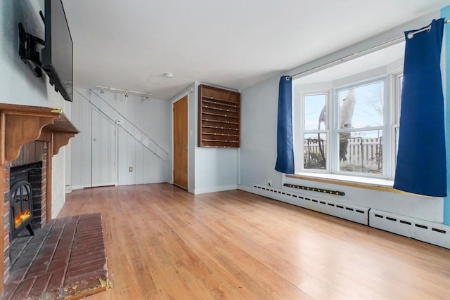 unfurnished living room with track lighting, a brick fireplace, wood finished floors, baseboards, and baseboard heating