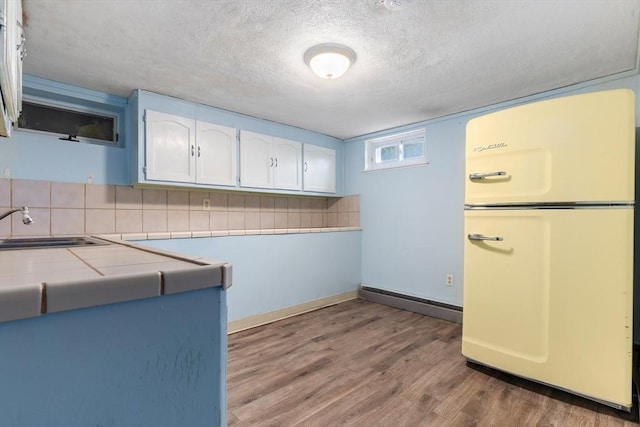 kitchen with white cabinets, tile counters, a textured ceiling, freestanding refrigerator, and wood finished floors