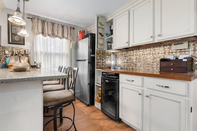 kitchen with decorative backsplash, freestanding refrigerator, white cabinetry, and a kitchen breakfast bar
