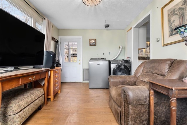living room featuring washing machine and clothes dryer, a textured ceiling, a healthy amount of sunlight, and light wood finished floors