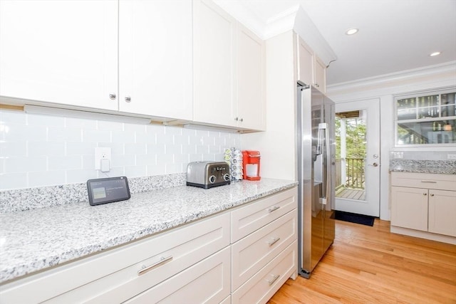 kitchen with stainless steel fridge, crown molding, and white cabinetry