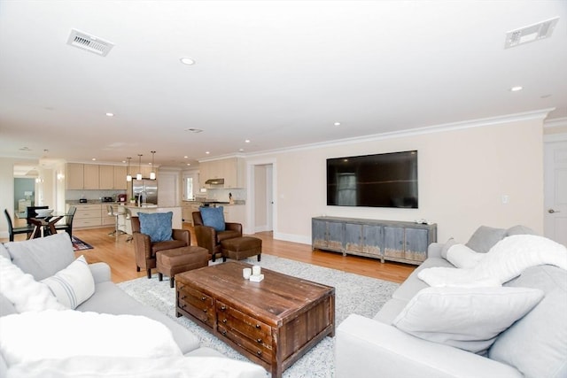 living area with ornamental molding, recessed lighting, visible vents, and light wood-style floors