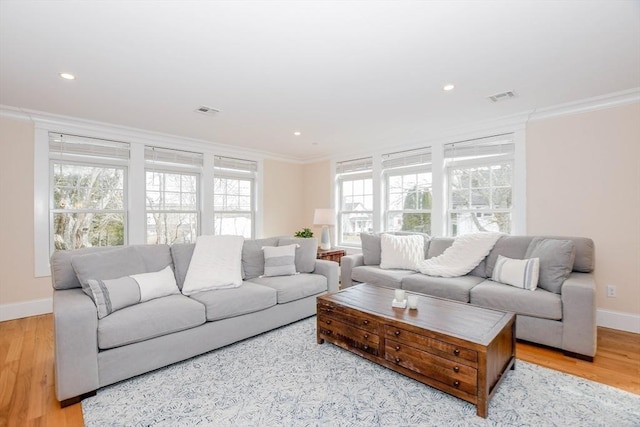 living room featuring ornamental molding, light wood-type flooring, visible vents, and baseboards