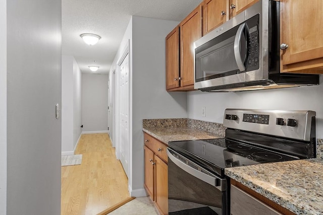 46 Ashford Unit 14, Methuen, MA 01844 - kitchen with appliances with stainless steel finishes, brown cabinets, light wood-style flooring, and light stone countertops