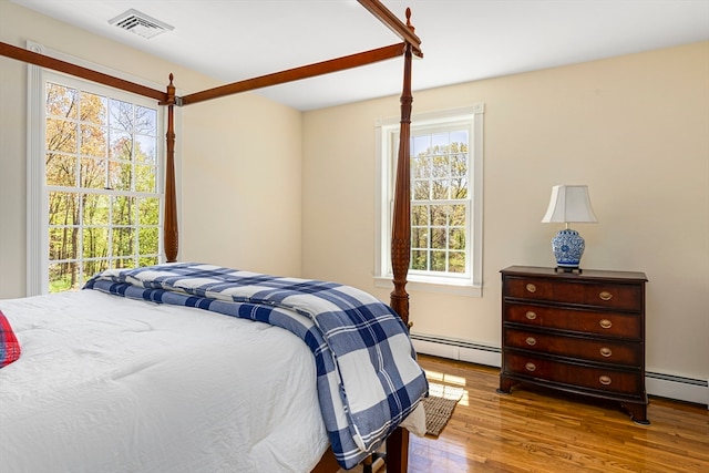 bedroom with baseboard heating, hardwood / wood-style flooring, and multiple windows